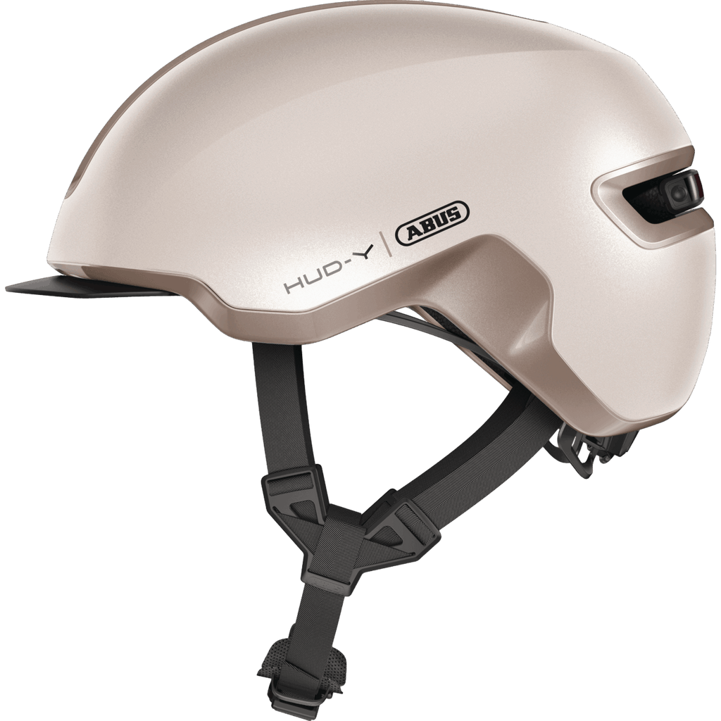 Ein stylischer Abus - Hud-Y Helm in Beige mit glatter Oberfläche, schwarzen verstellbaren Riemen, Fidlock-Verschluss und einer USB-LED-Rückleuchte. Das "Abus"-Branding befindet sich an der Seite.