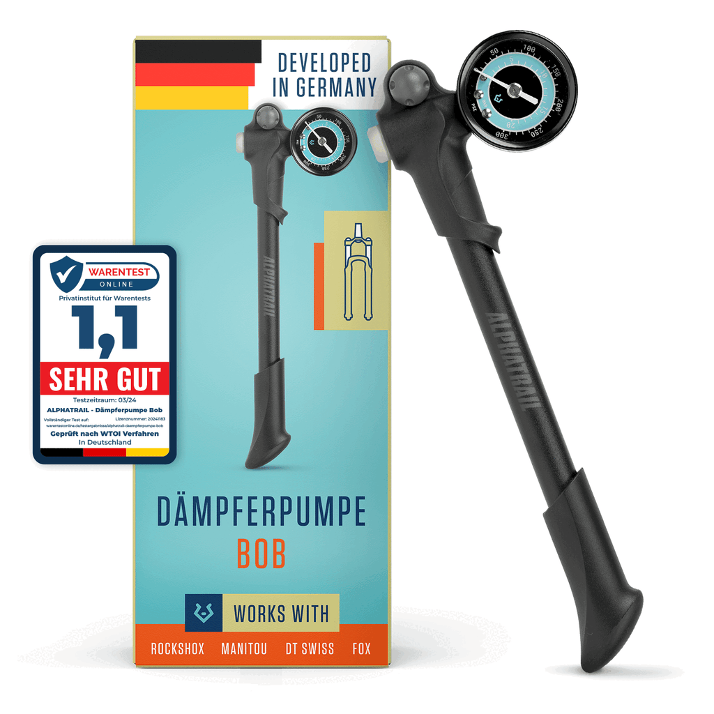 Eine schwarze Alphatrail Dämpferpumpe Bob steht vor ihrer deutschen Alphatrail-Verpackung. Sie ist mit einem Manometer ausgestattet, passt für RockShox, Manitou, DT Swiss und Fox Dämpfer und hat links eine 1.1 "SEHR GUT"-Plakette.